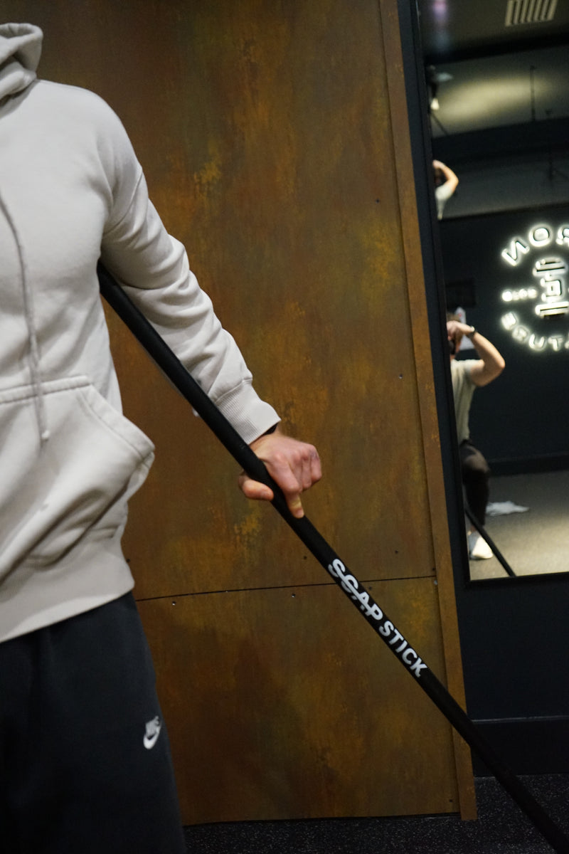 Athlete holding SCAP Stick recovery tool in gym - shoulder impingement relief and muscle therapy
